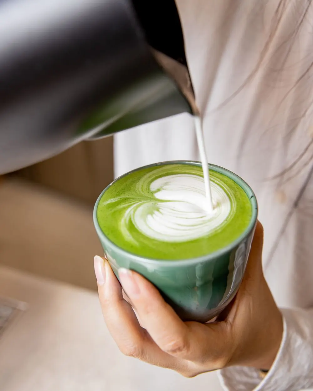 Preparing matcha latte with latte art in a ceramic cup.