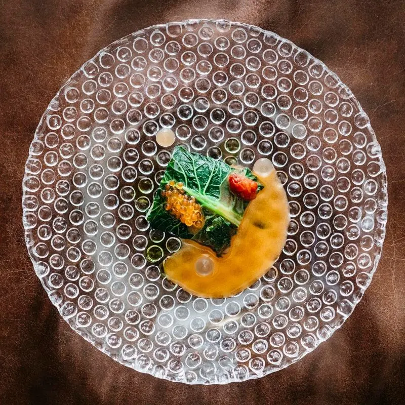 Fine dining dish detail served on a textured glass plate with bubble pattern.