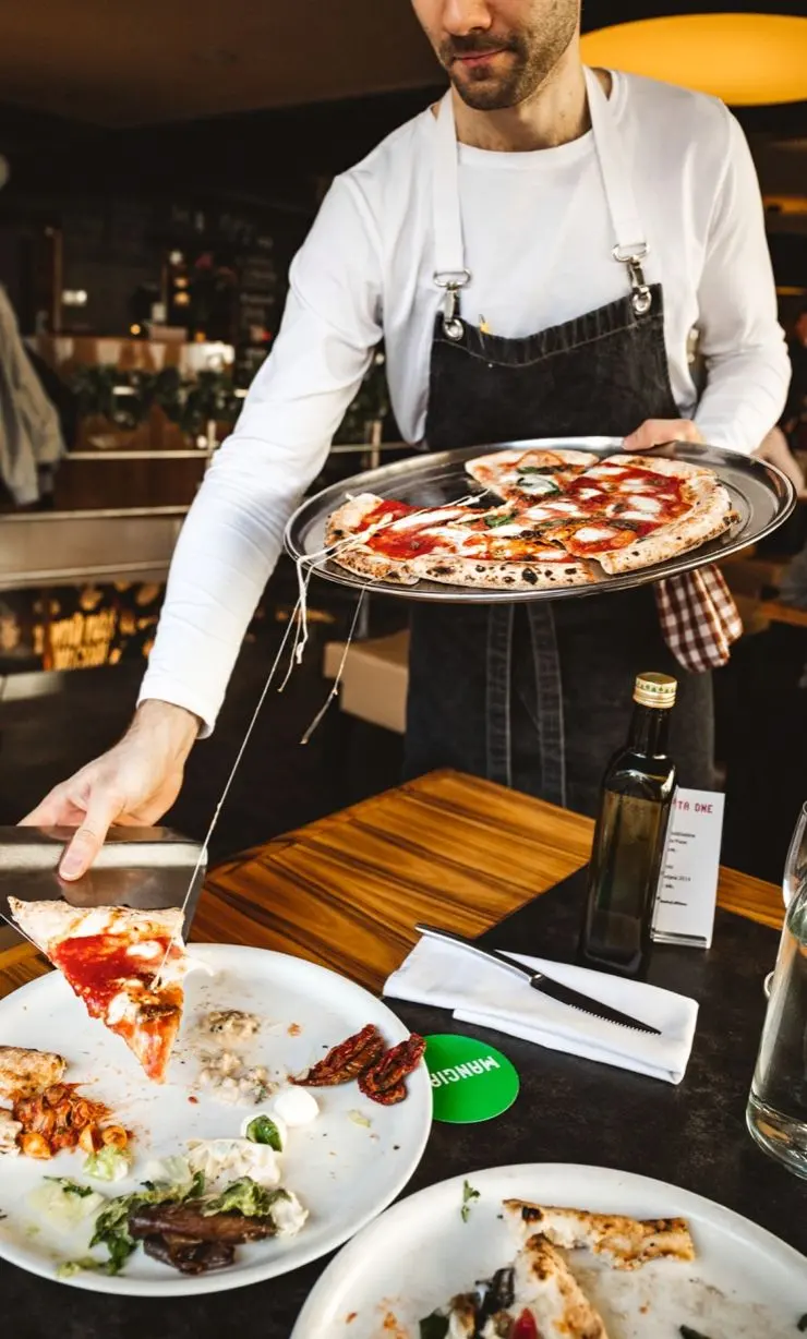 Waiter serving fresh Italian pizza in Pizza Nuova restaurant.