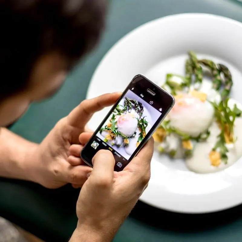 Food photography with a smartphone – close-up of hands taking a photo of a modern plated dish.