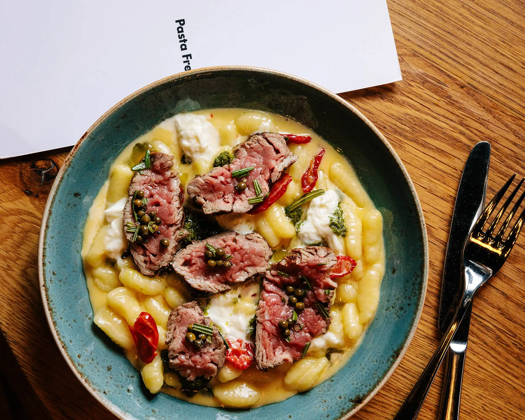 Talíř s těstovinami a plátky masa v restauraci Pasta Fresca.