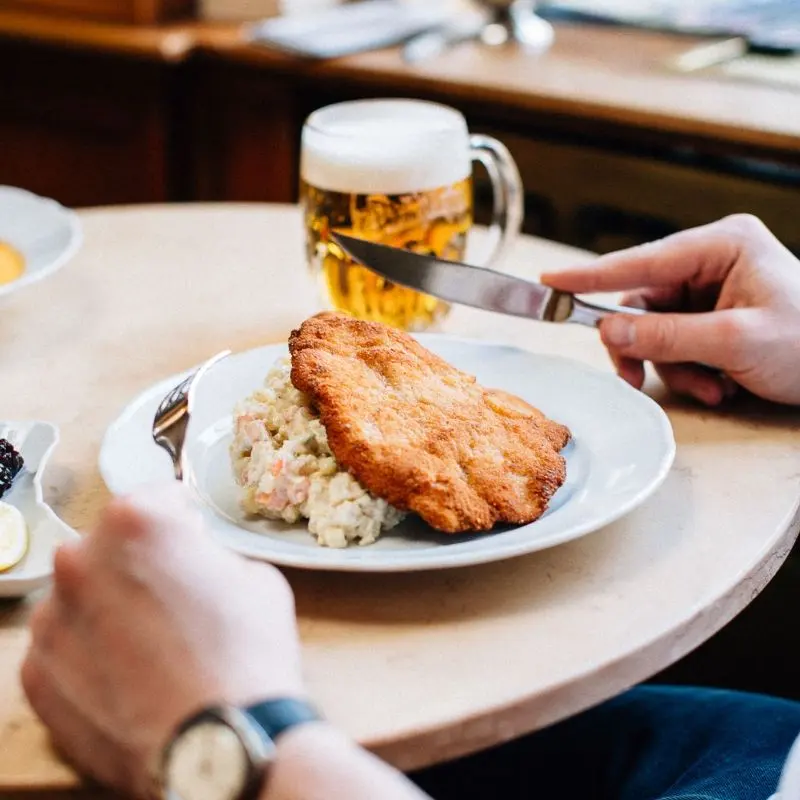 Fried schnitzel with potato salad on the table, with a glass of beer behind it.