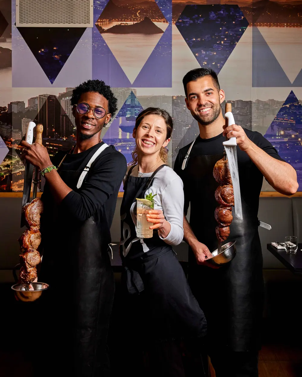 Restaurant team holding grilled meat skewers and a cocktail.