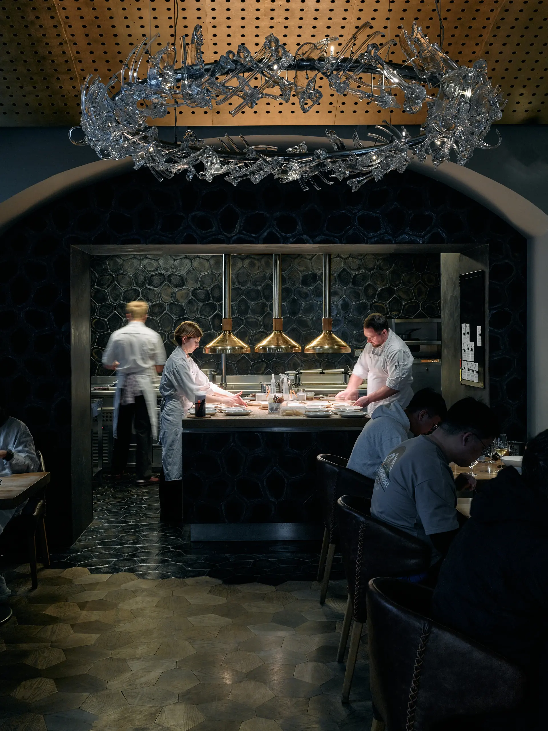 Interiér restaurace La Degustation Bohême Bourgeoise v Praze s otevřenou kuchyní a šéfkuchaři při práci.